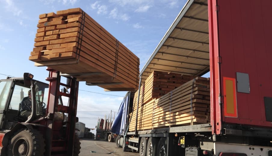 A forklift loading banded timber into a curtain-side trailer at a freight yard